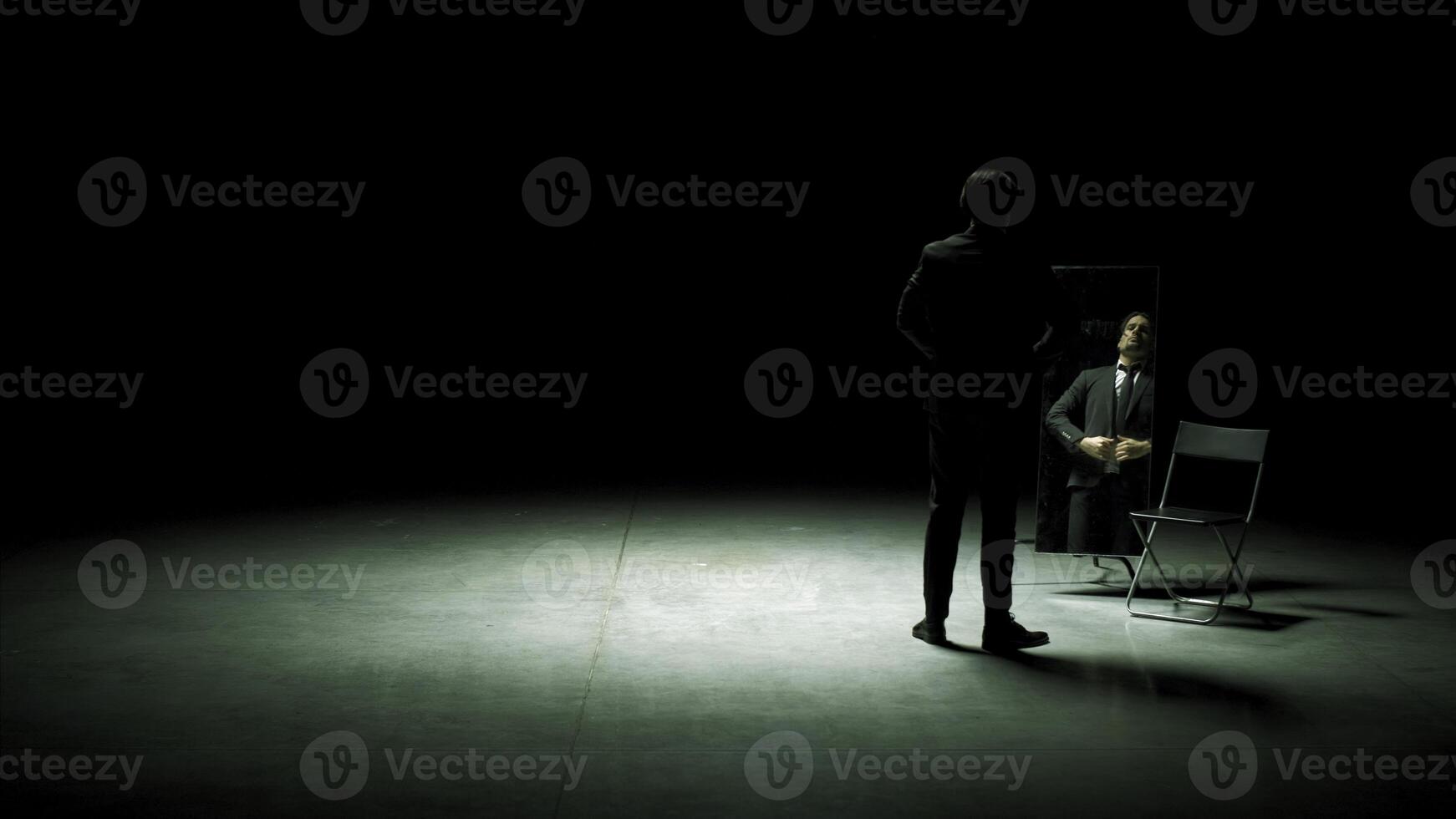 Man in suit in front of mirror. Stock footage. Man on stage with mirror puts on suit. Stage production with one man and mirror on dark stage photo