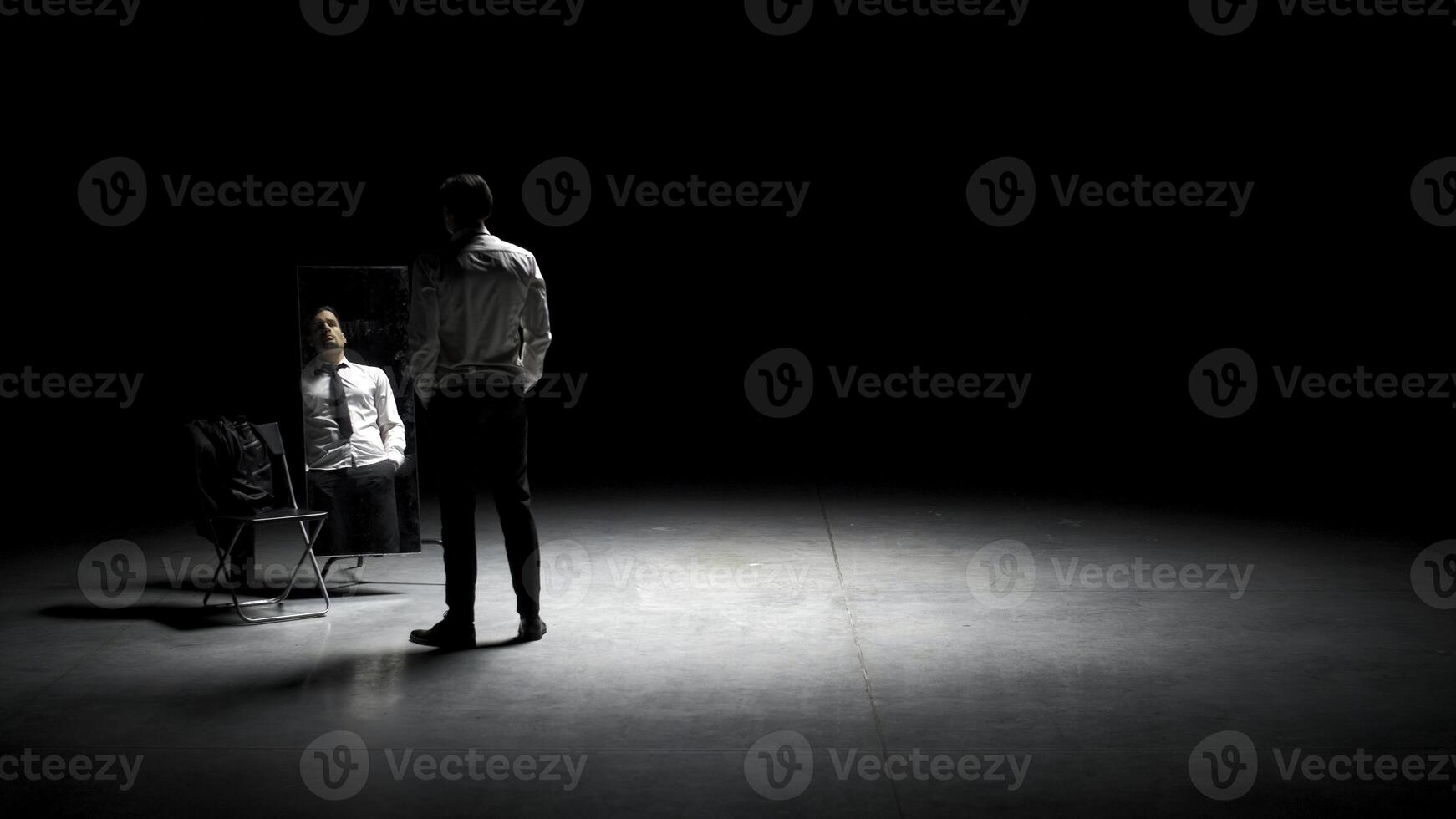 Man in suit in front of mirror. Stock footage. Man on stage with mirror puts on suit. Stage production with one man and mirror on dark stage photo