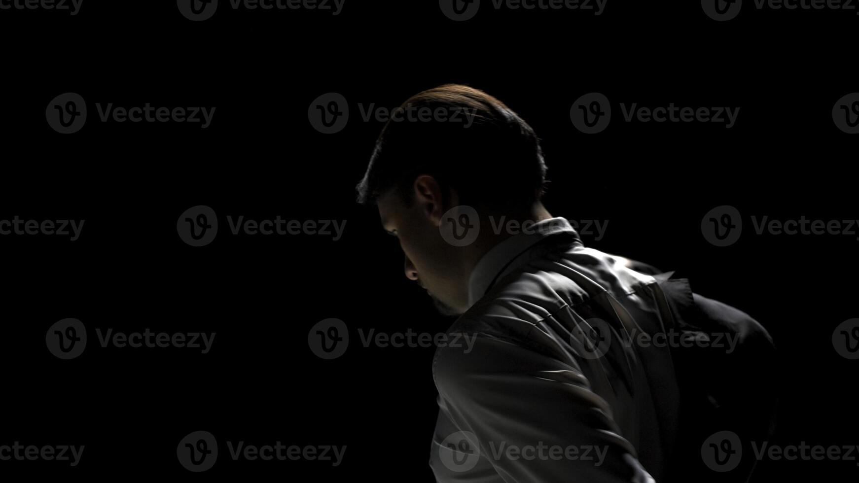 Rear view of attractive man putting on suit. Stock footage. Man takes jacket from chair and puts it on in front of mirror. Man wears costume on theatrical stage in single production photo