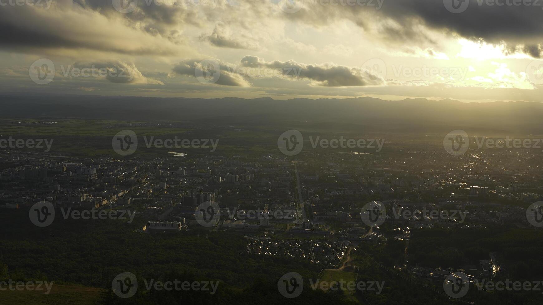 Top view of city in green valley with sun on horizon. Clip. Beautiful landscape of sunny green valley with town on summer day. Bright sun shines down on valley with town photo