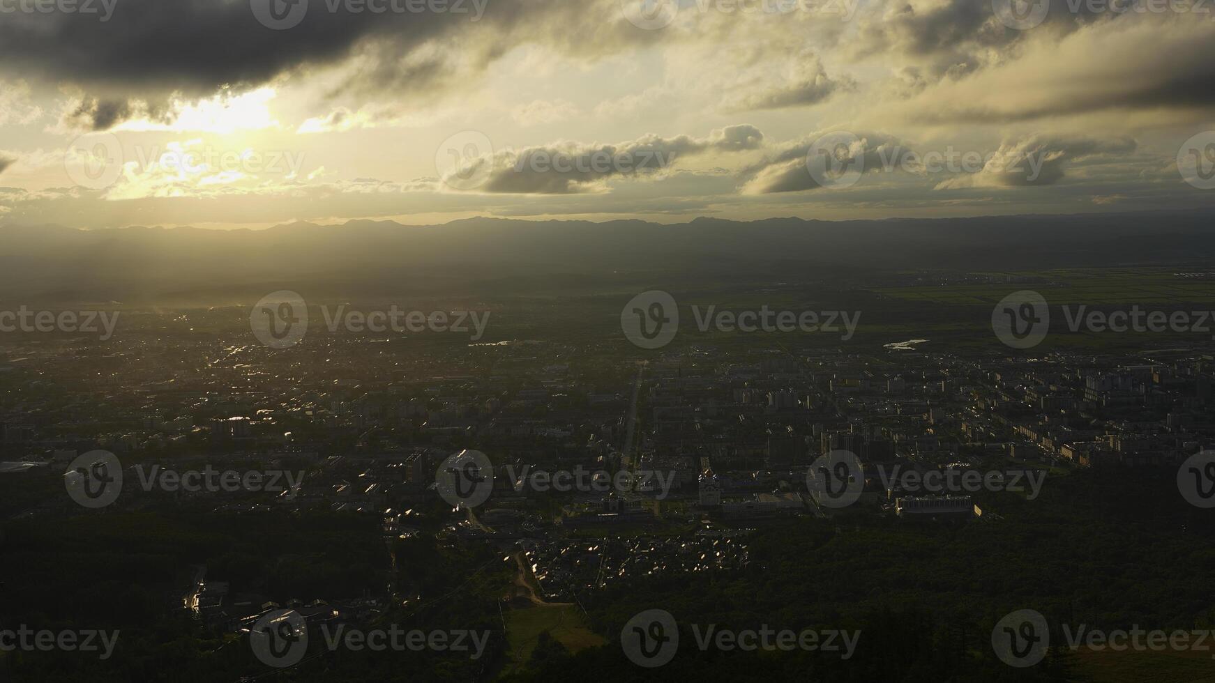 Top view of city in green valley with sun on horizon. Clip. Beautiful landscape of sunny green valley with town on summer day. Bright sun shines down on valley with town photo