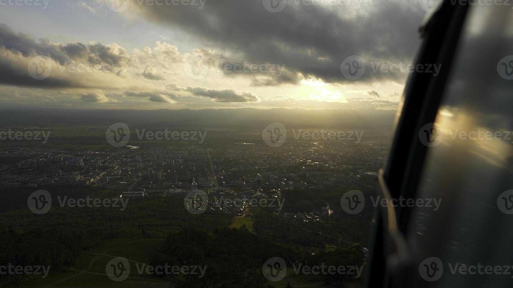 Top view from cab of cable car on town. Clip. Beautiful landscape on small town in green valley on sunny day. Sunny view opens from rising cab of cable car photo