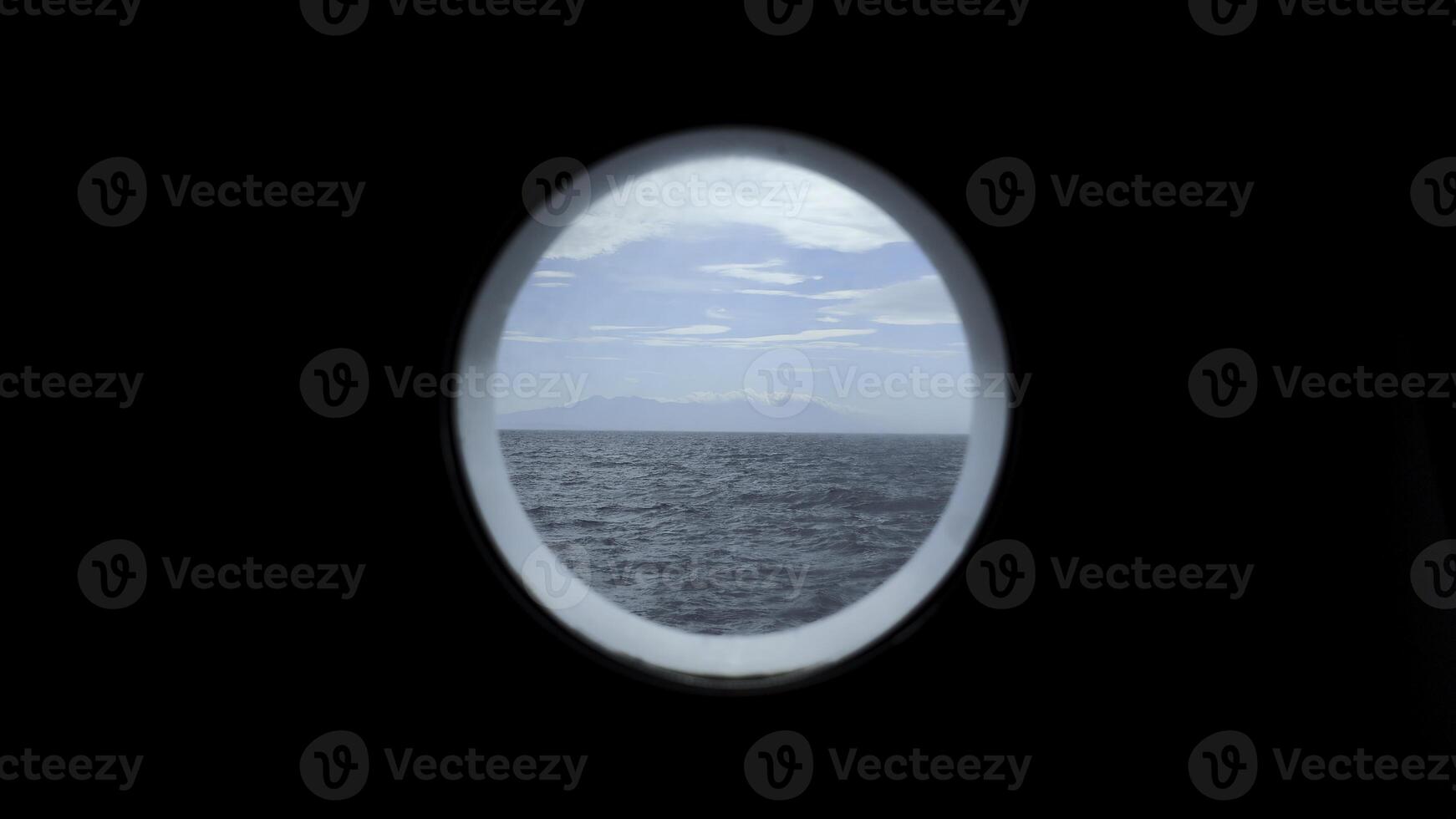 View from round deck window to sea. Clip. Beautiful seascape with mountain coast on horizon from round window. Sea voyage and view from round window photo