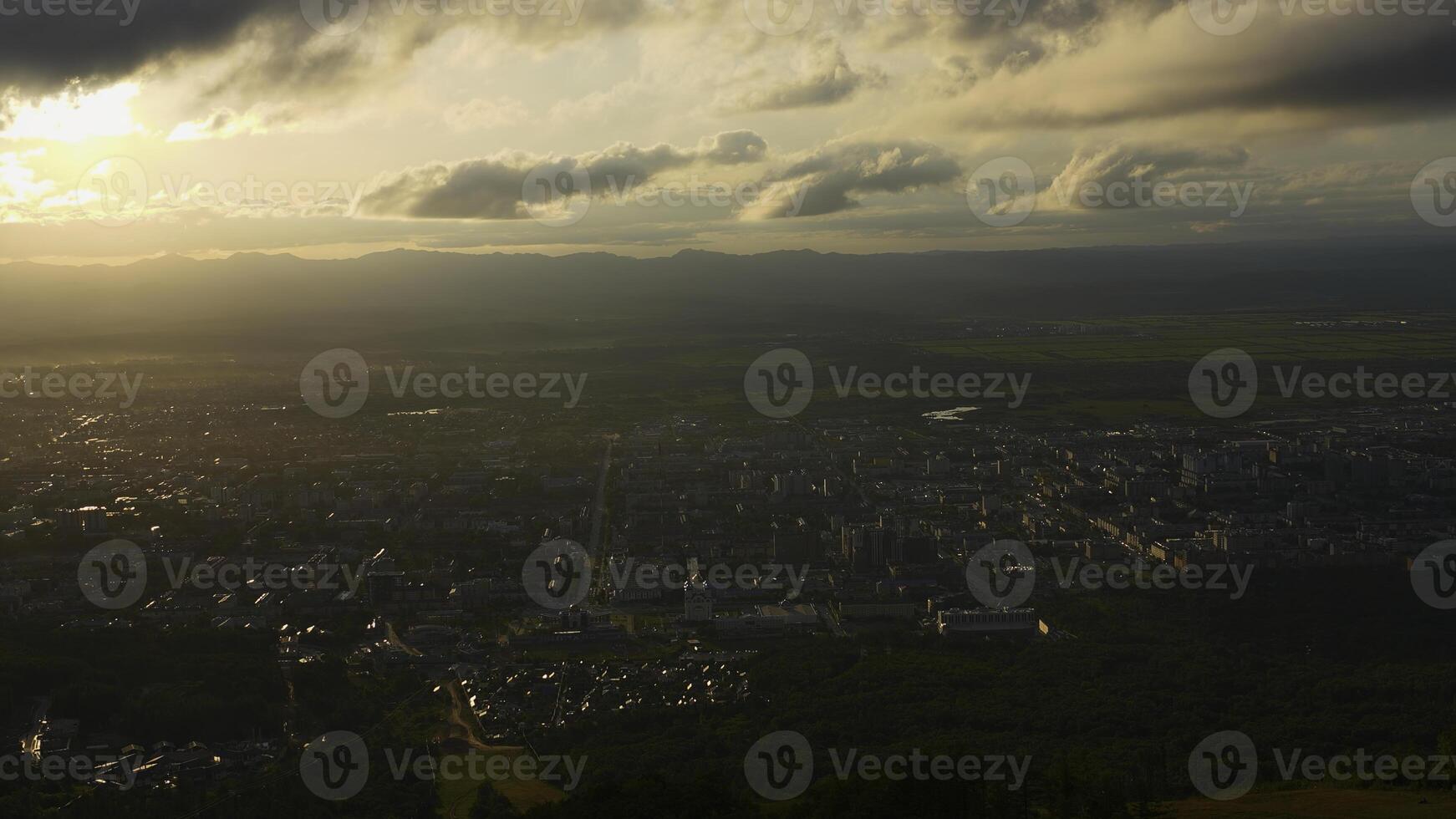 Top view of city in green valley with sun on horizon. Clip. Beautiful landscape of sunny green valley with town on summer day. Bright sun shines down on valley with town photo