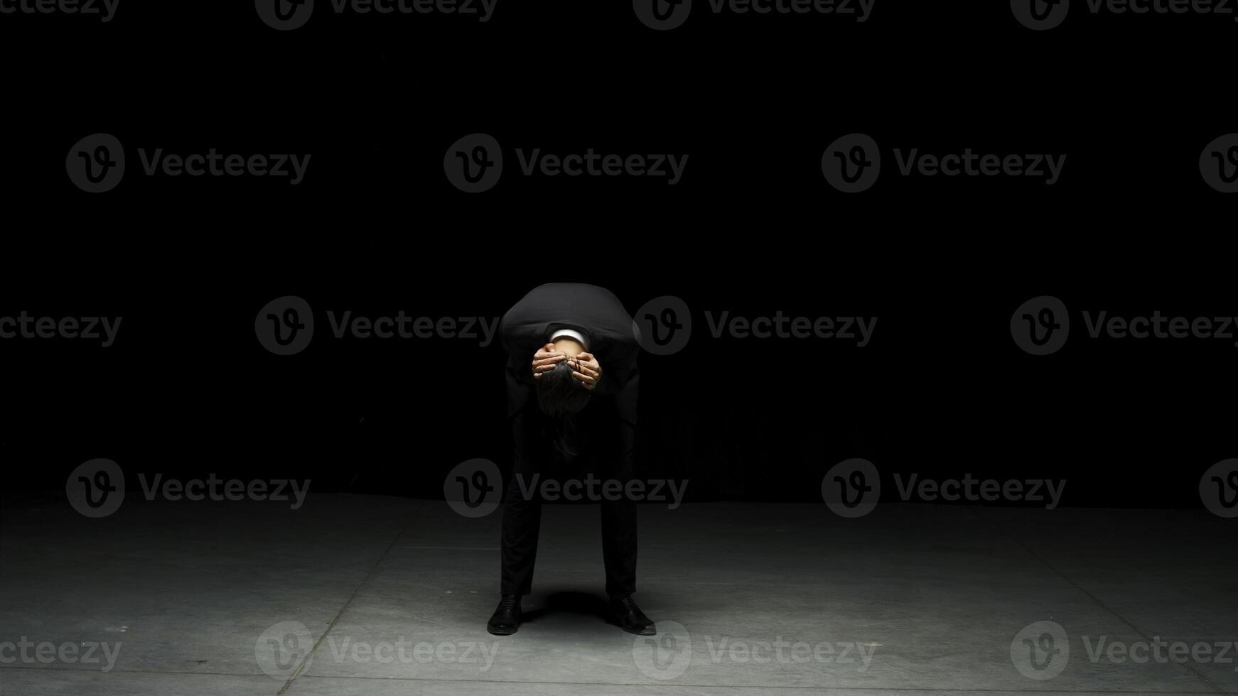 Man in suit stands emotionally on stage. Stock footage. Man in suit stands on stage with dramatic look. Elegant dramatic man on dark stage in emotional production photo