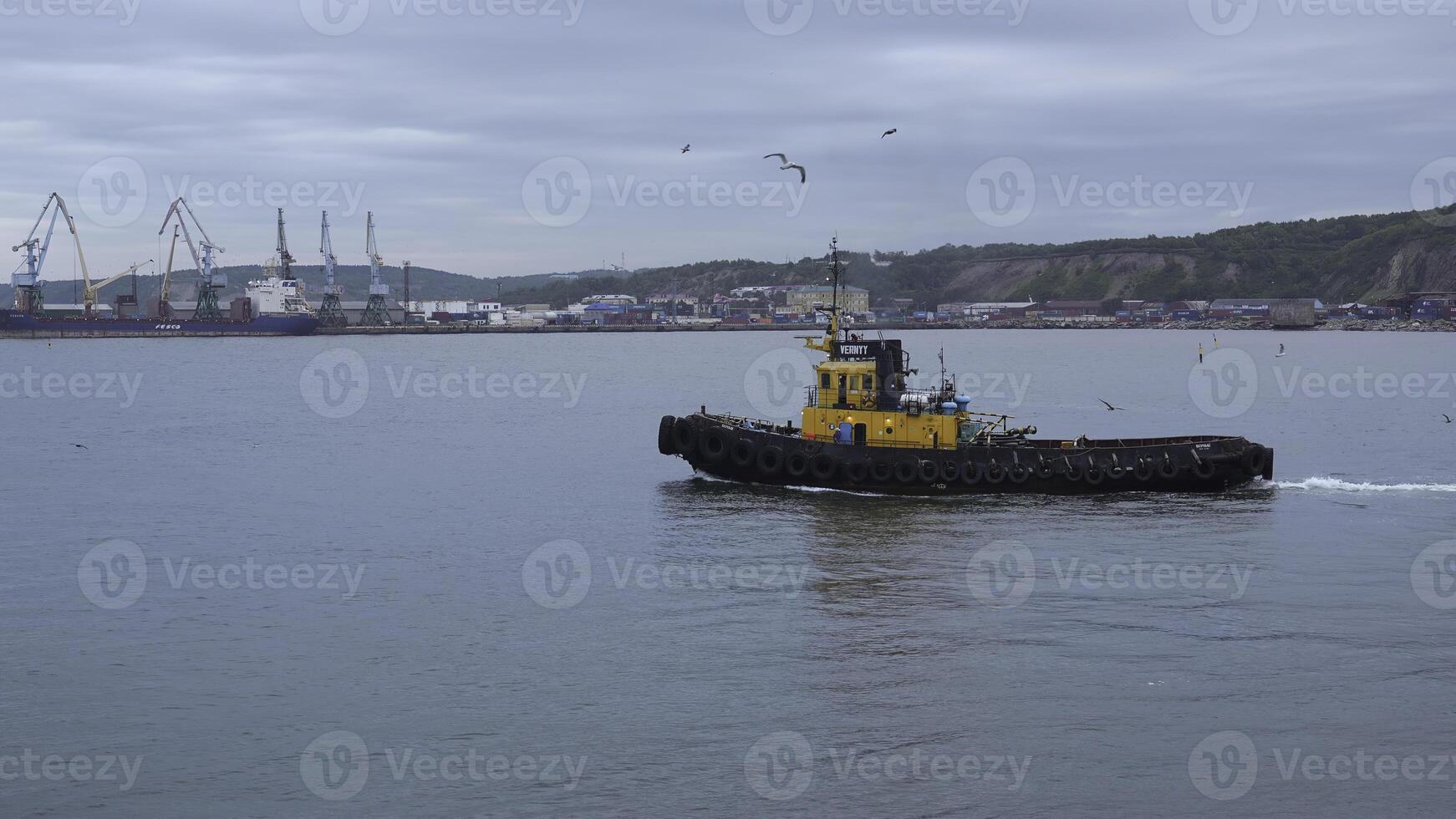 Fishing boat on background of port in cloudy weather. Clip. Fishing vessel sails out of seaport into sea. Fishing boat sails into sea on cloudy day photo