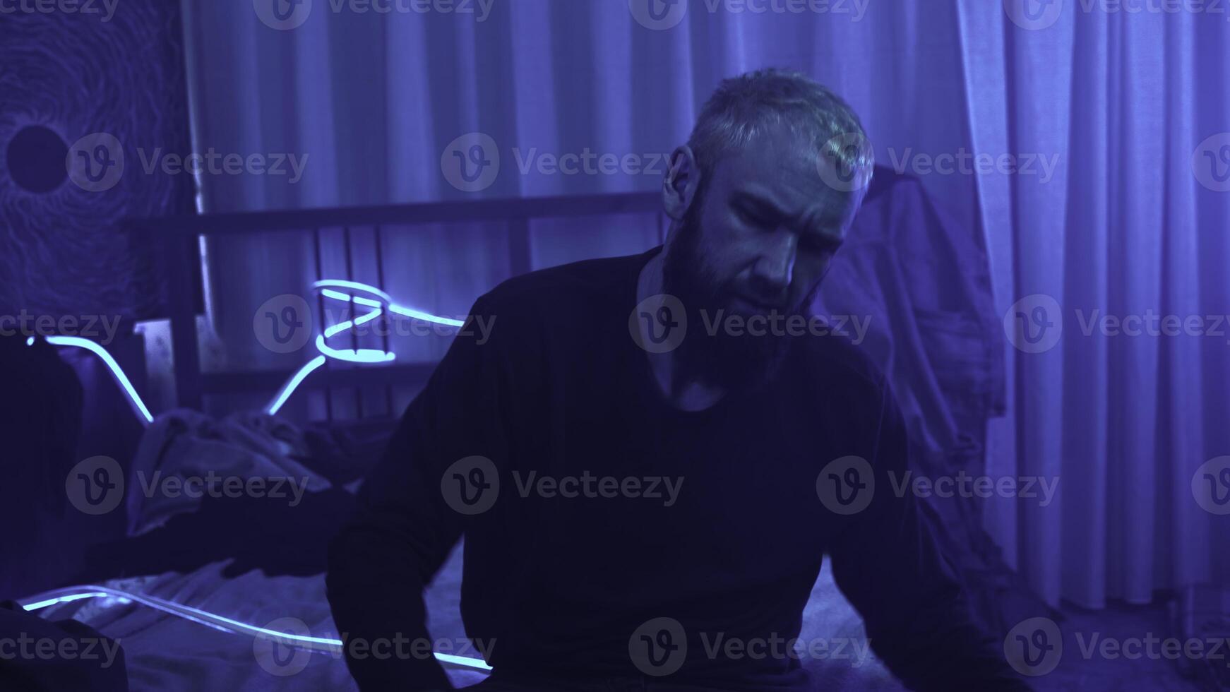 Man is getting emotional in neon room. Media. Man vividly shows aggressive emotions alone at home. Man with panic anxiety and outbursts of anger in neon room. Outbursts of emotion photo
