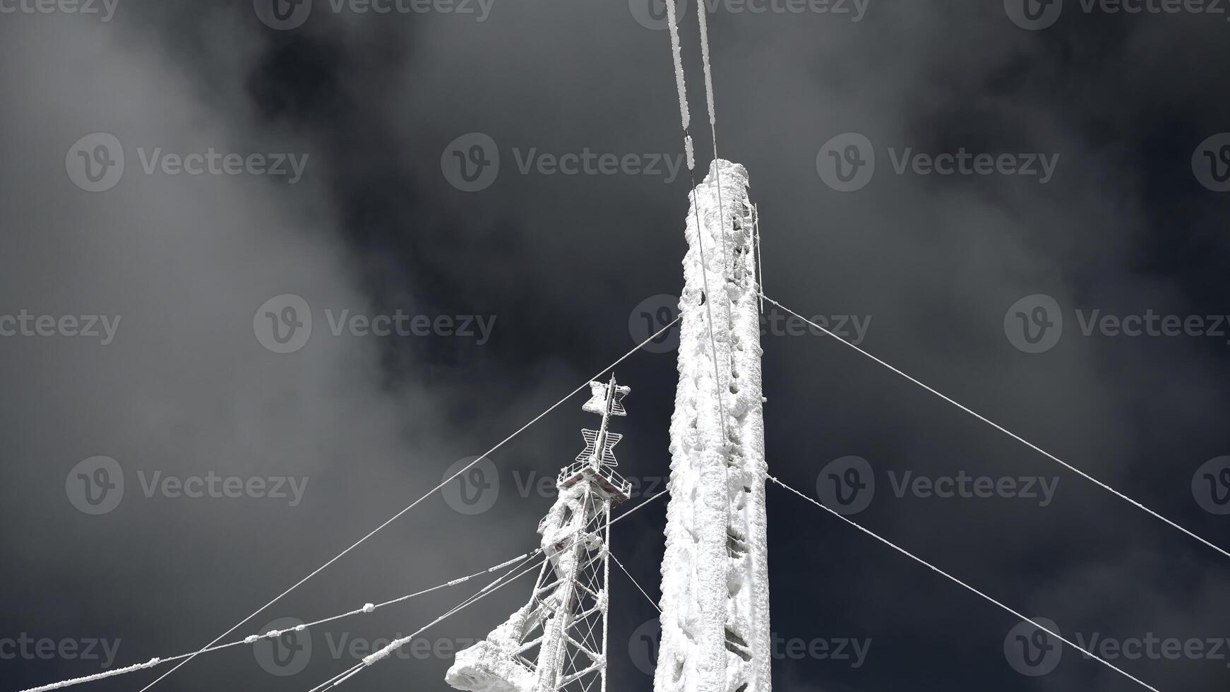 Snow-covered radio tower on background sky. Clip. Frozen structure of electric tower in winter. Radio towers covered with snow on sunny winter day photo