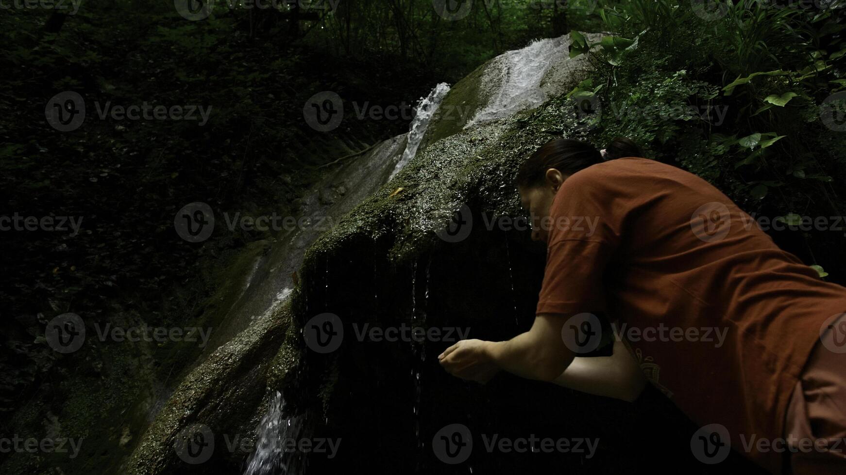 Young woman drinking water from cascade waterfall at deep tropical rain forest. Creative. Female hiker drinking water from mountainous spring. photo