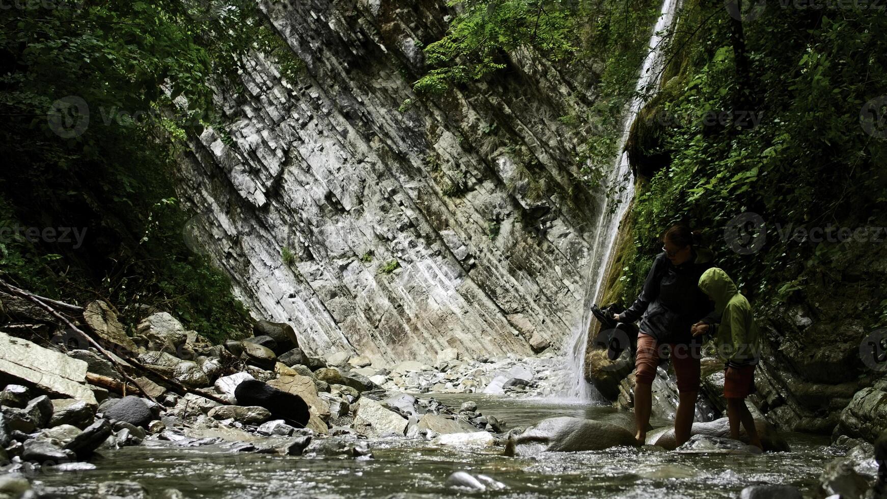 Mother and boy crossing mountain cold water stream with stones. Creative. Hikers in picturesque place. photo