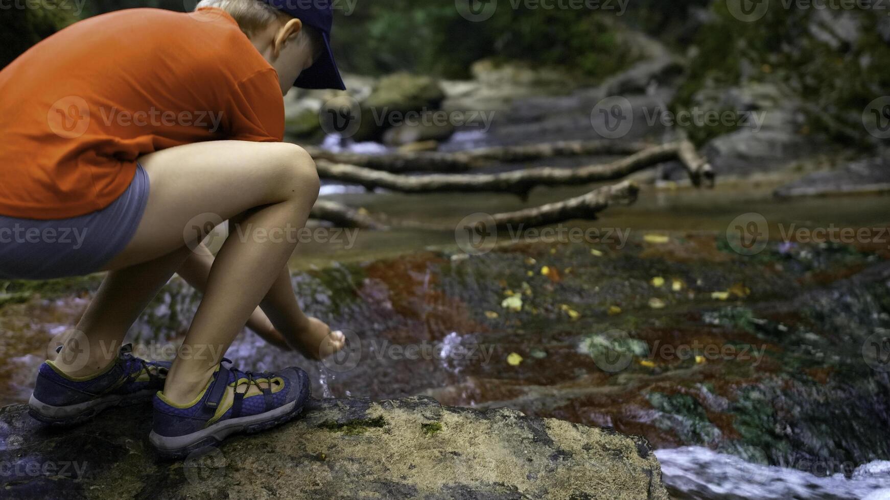 turista chico pone su manos en el río a bebida frío claro agua. creativo. joven chico Bebiendo agua desde primavera. foto