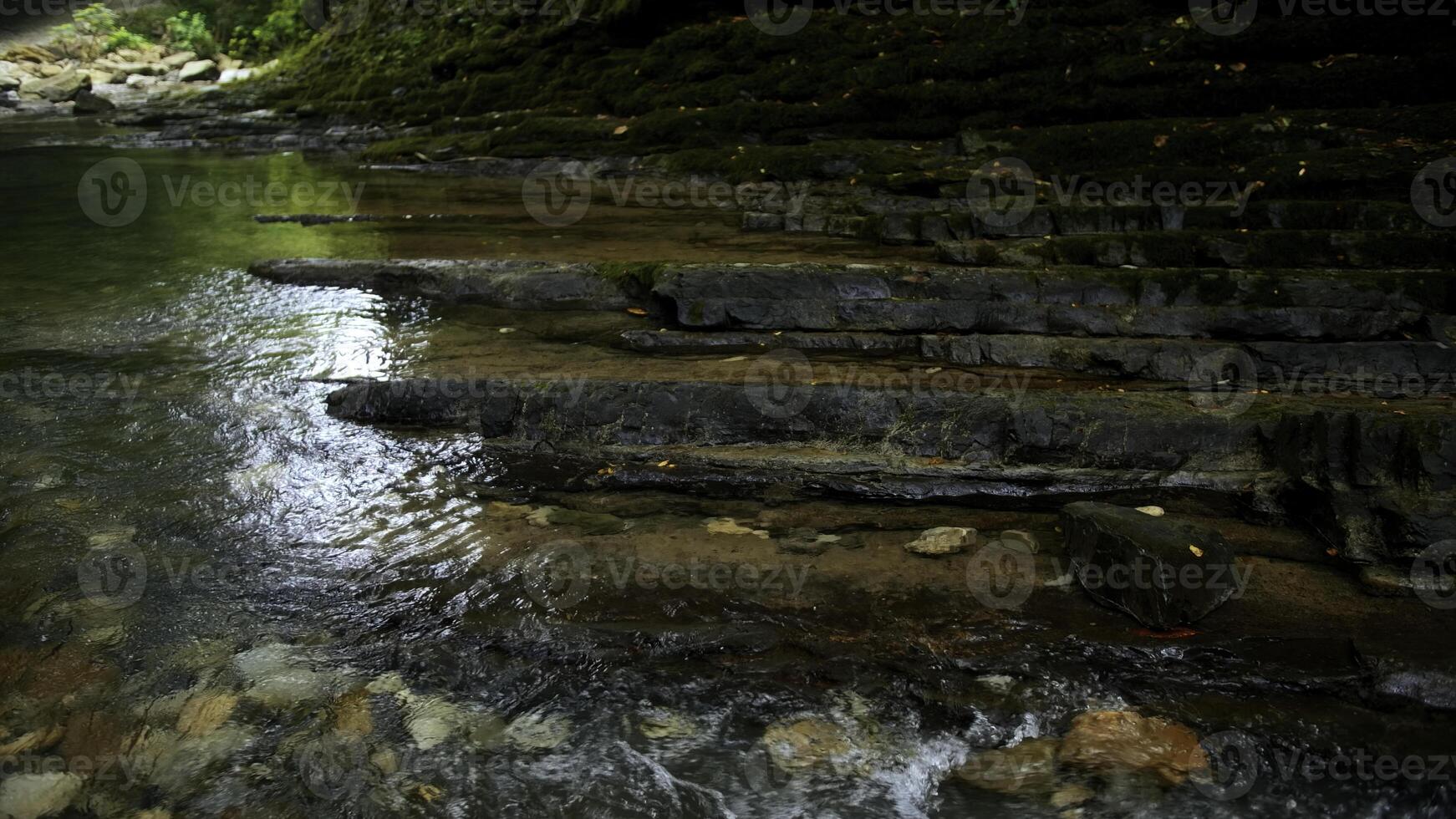 Clear stream running through stone boulders. Creative. Calm river flowing on stone bottom in slow motion. photo