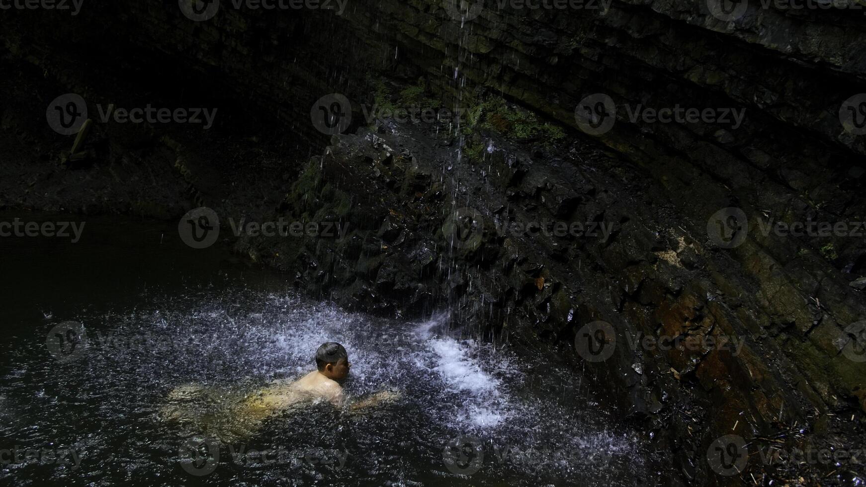 Child boy swimming in mountain pond with waterfall. Creative. Child on summertime vacation refreshing in river. photo