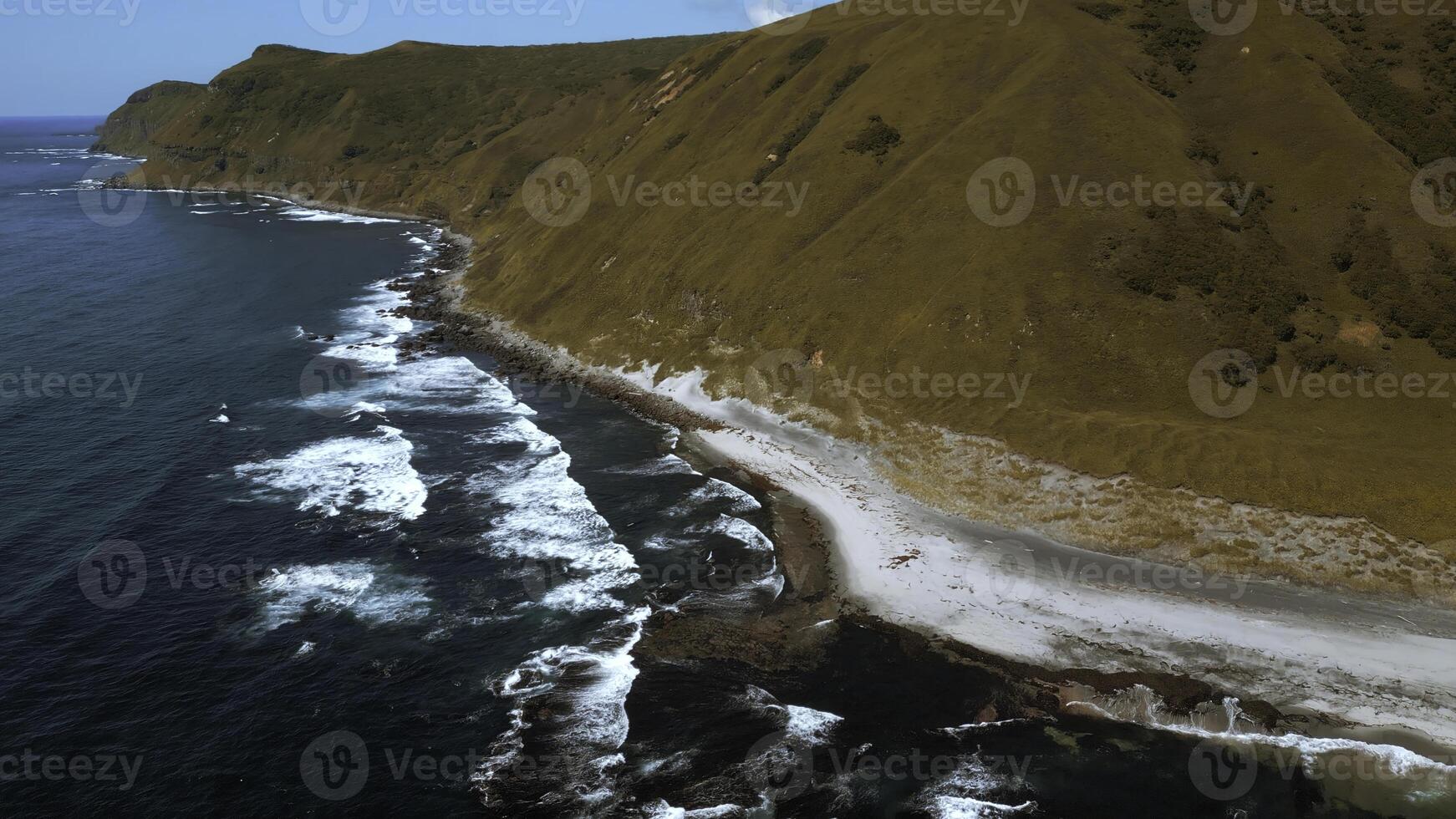 Aerial of mountain covered by burnt yellow grass and blue sea. Clip. Steep slope of yellow hill and dark blue waves crashing in stones and creating foam. photo