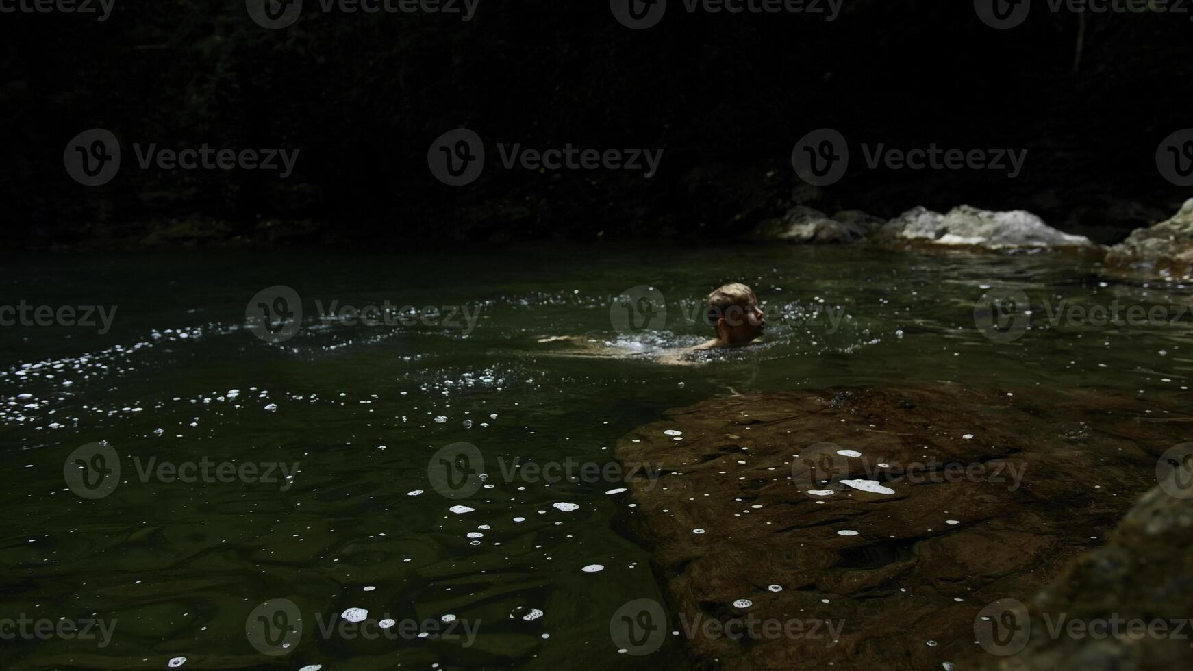 lento movimiento de un chico saltando dentro un cascada y natural estanque. creativo. joven chico niño teniendo divertido en selvas. foto