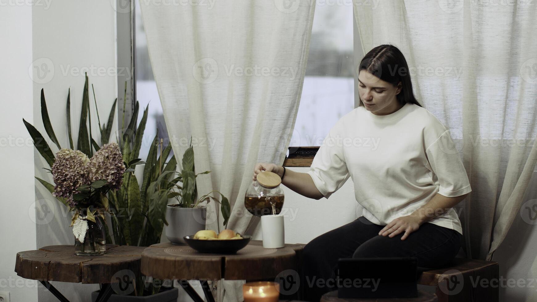 Young woman drinking tea in a kitchen at home. Media. Attractive lady enjoying cup of green tea and watching movie on tablet. photo