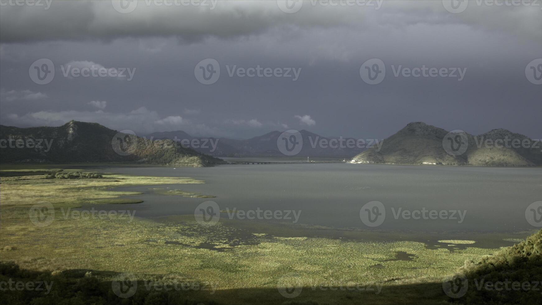 Sun and shadow on green meadow and a lake. Creative. Calm water and mountains on cloudy sky background. photo