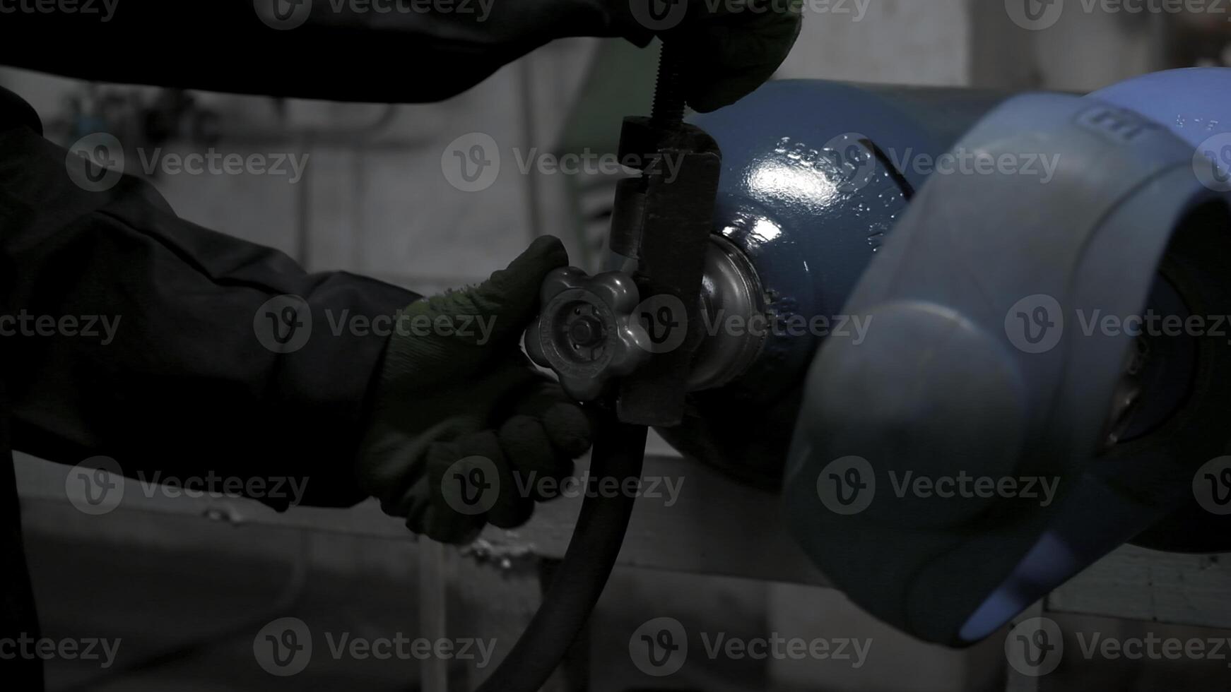 Close up of worker in gloves turning gas cylinder valve. Clip. Industrial background of the factory. photo