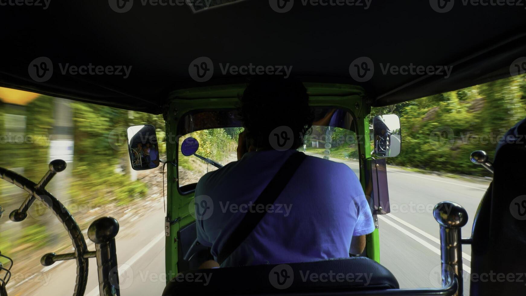 Rear view of a tuk-tuk or motorcycle driver carrying passengers along green trees and cars. Action. Concept of travelling. photo