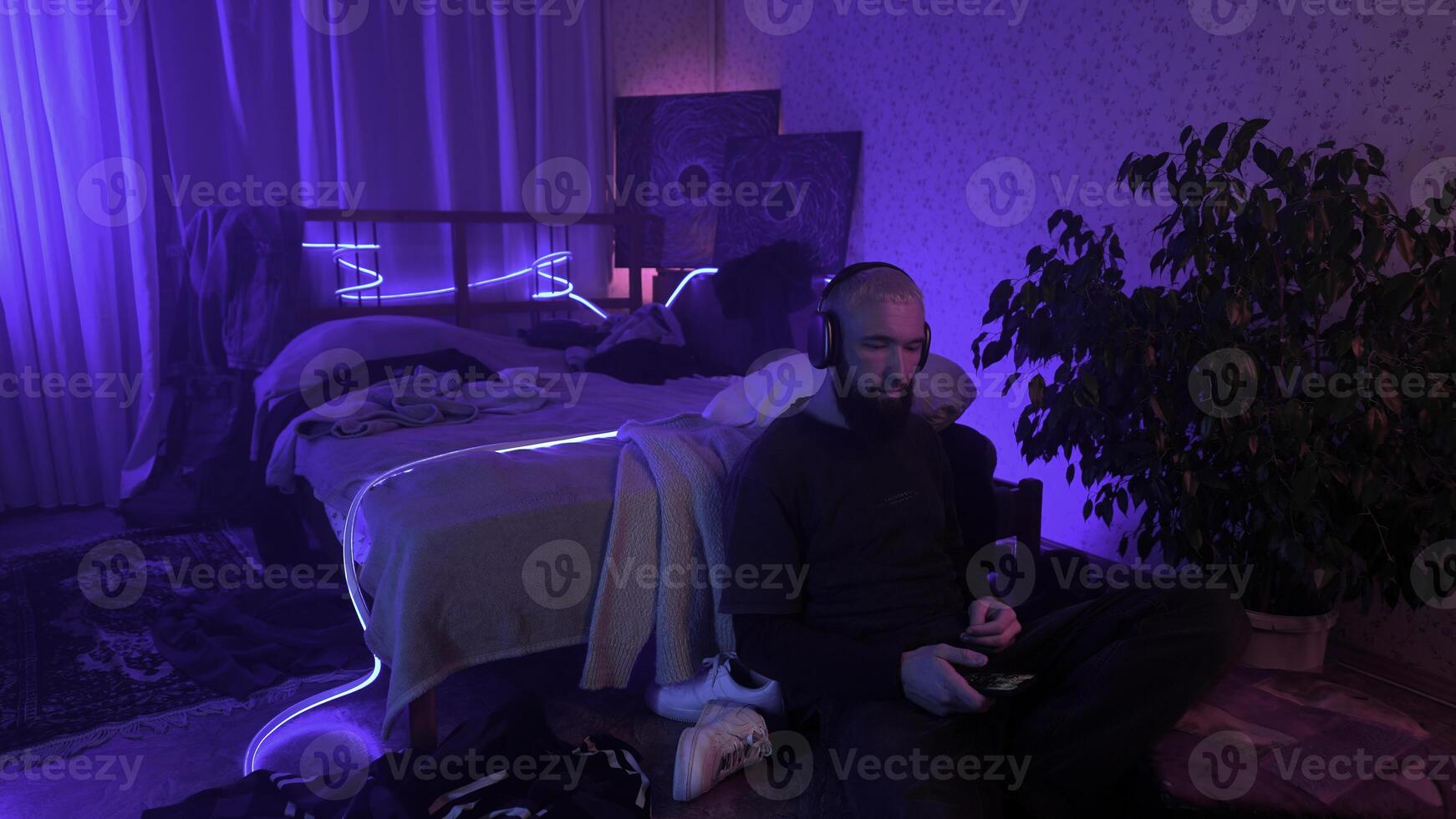 hombre utilizando teléfono inteligente y escuchando a música a hogar. medios de comunicación. acogedor y sucio habitación de un hipster chico. foto