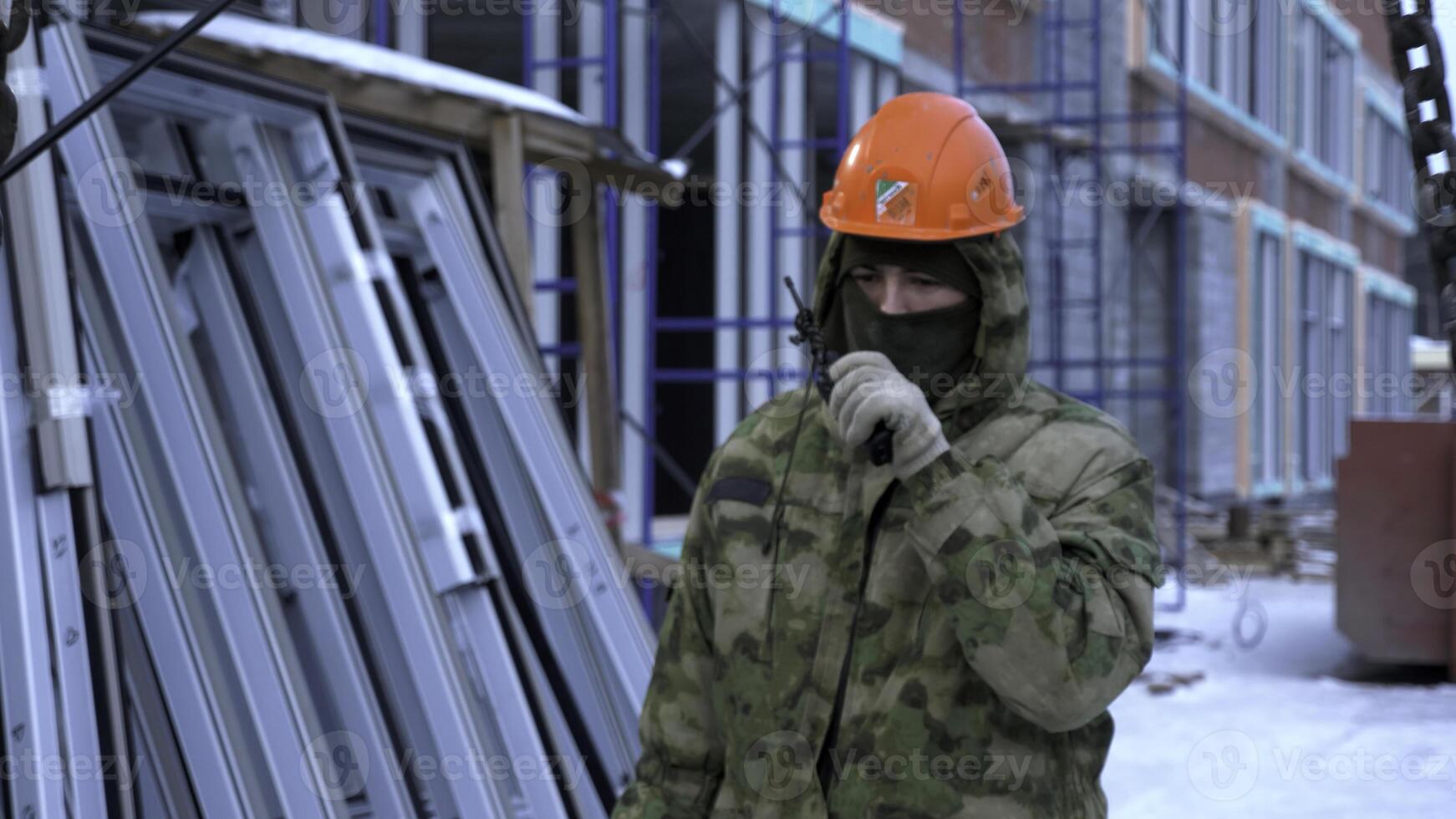 Worker using portable radio and hanging chains of crane on building site. Clip. Construction of the residential buildings, high rise residential complex under construction. photo