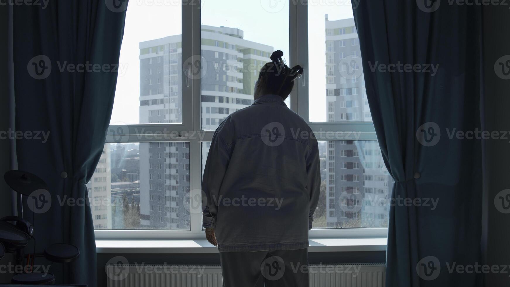 Young woman enjoying view through the panoramic window in the morning at home. Media. Girl in pajamas standing and thinking by the window in bedroom. photo