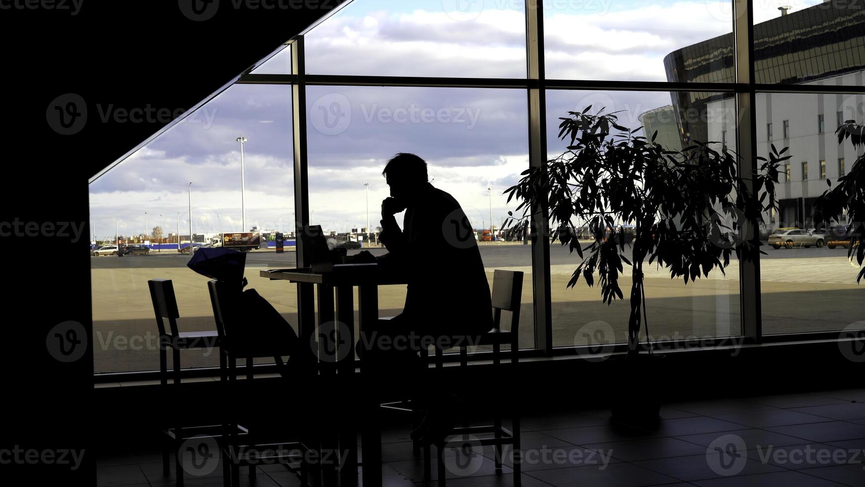 Businessman waiting for boarding at the airport and looking through panoramic windows. Silhouette of a man at a table with shadows of passing people. photo