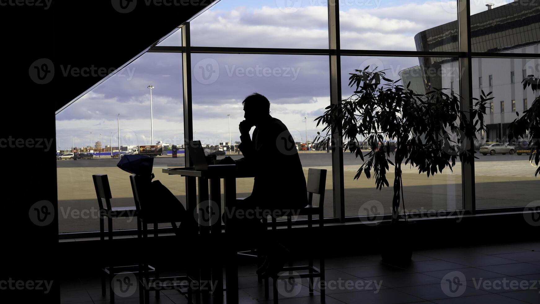 Businessman waiting for boarding at the airport and looking through panoramic windows. Silhouette of a man at a table with shadows of passing people. photo