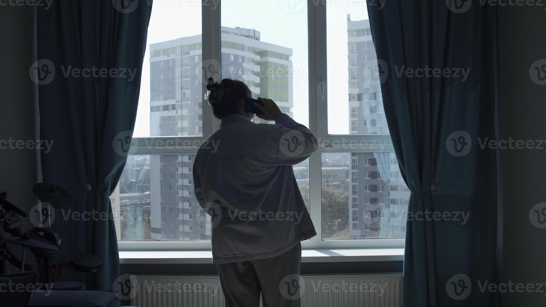 Rear view of a woman talking on a cell phone by the window. Media. Woman in pajamas talking on smartphone at home. photo