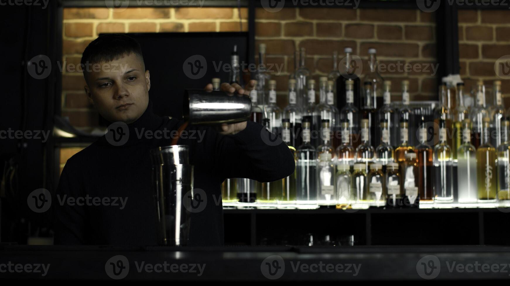 el barman preparando Perfecto cóctel, en pie detrás el bar encimera. medios de comunicación. muchos botellas de alcohol en el antecedentes. foto