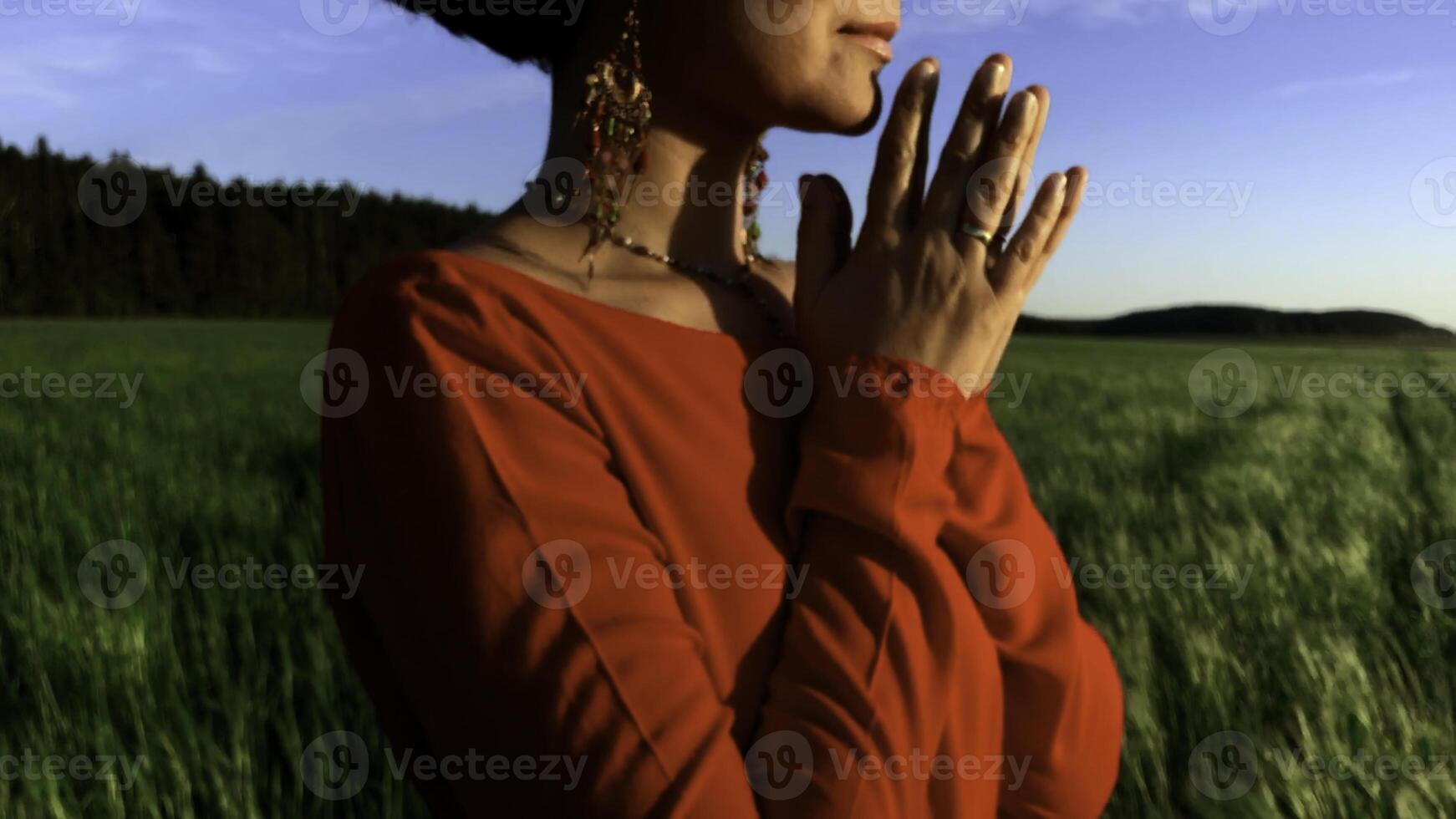 joven bonito niña mujer meditando con cerrado ojos. valores acortar. Orando mientras en pie en un campo con un hermosa ver en un Ventoso verano día a puesta de sol. foto