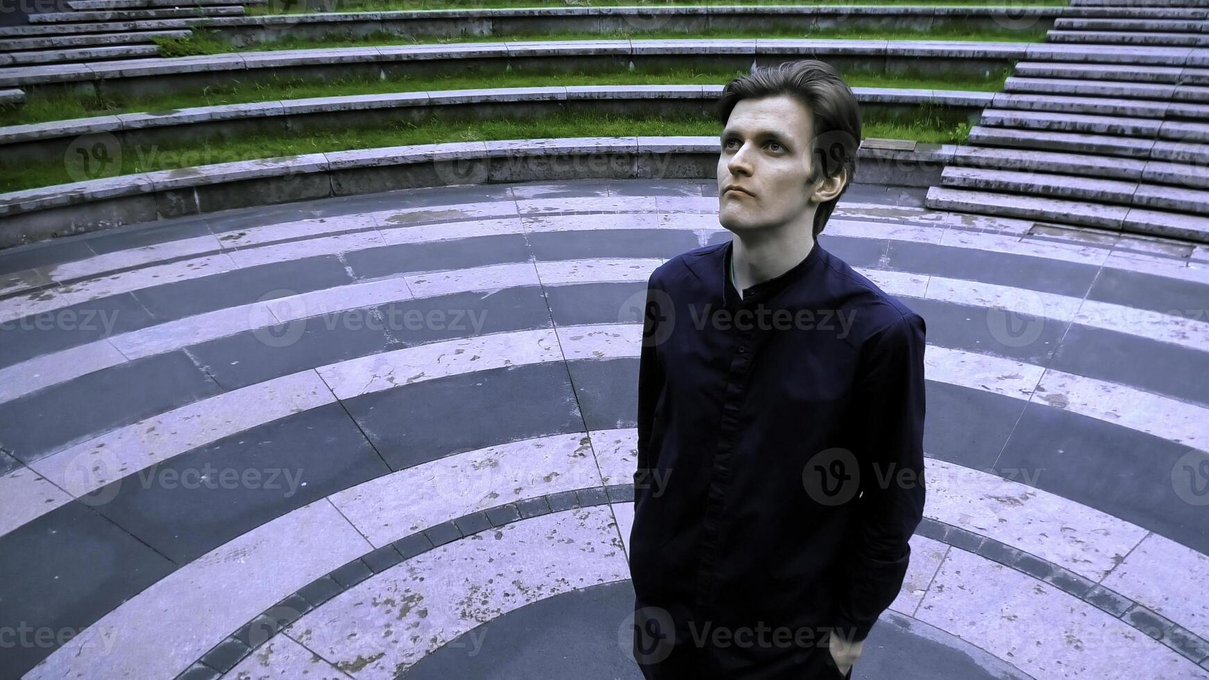 Tall man in black clothes standing in the meddle of amphitheater. Stock clip. Asphalt colored in black circles. photo