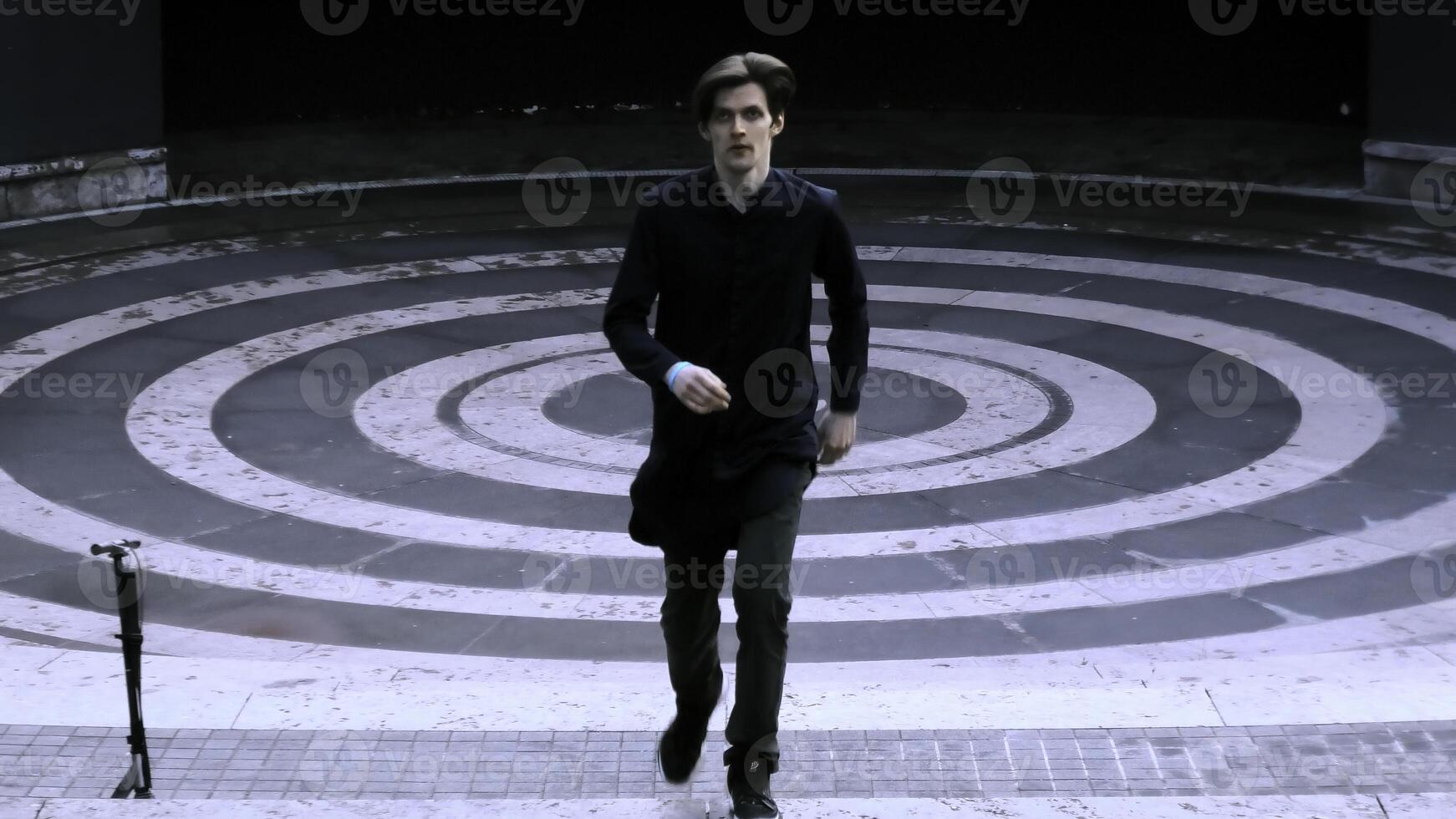 Young man dressed in black running up the stairs of stone amphitheater. Stock clip. Asphalt painted in white and black rings. photo