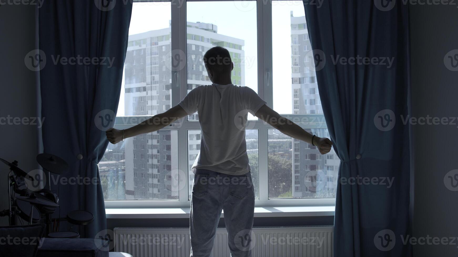 Early morning, silhouette of man exercising, stretching body by window at home. Media. Rear view of a young man standing against window. photo