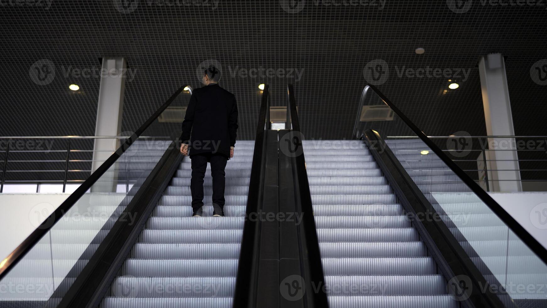 Passenger riding on the escalator up to the station of the ground metro. Media. Rear view of a young businessman on the escalator. photo