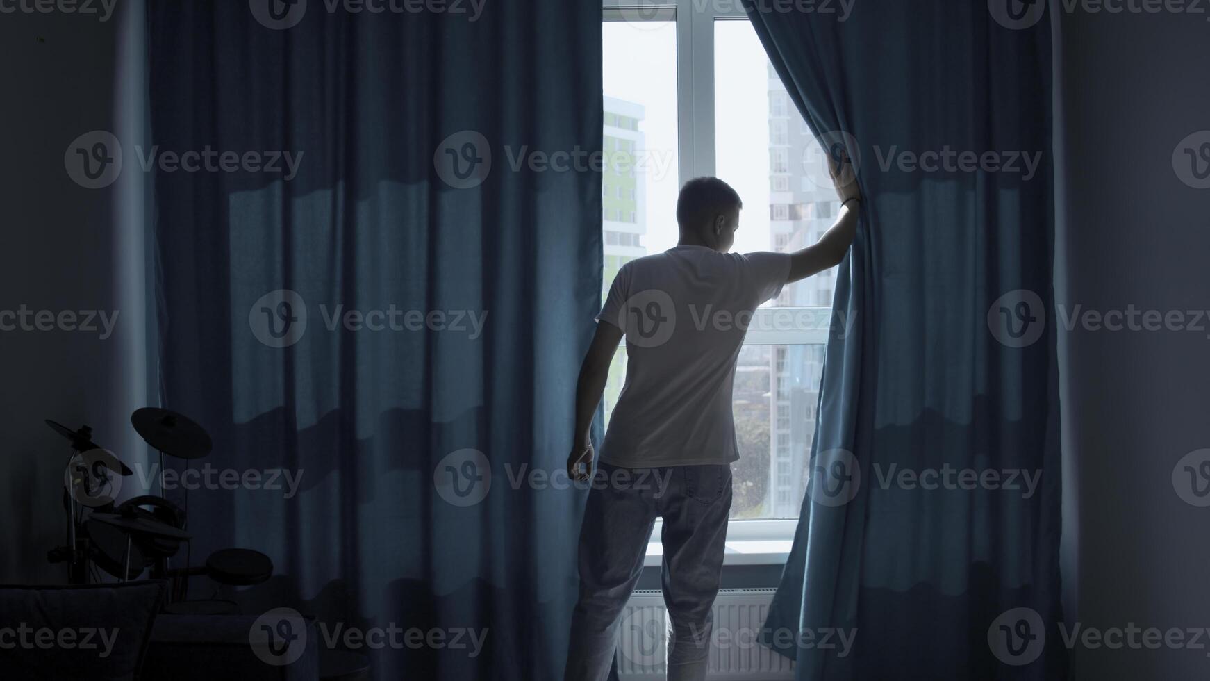 Early morning, a man coming to the window and pulling the curtains apart. Media. Looking at the city panorama from a high floor and thinking about the coming day. photo