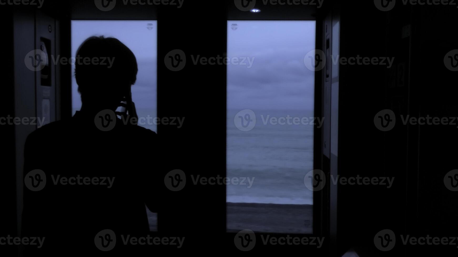 Young tourist with a smartphone looks out of the window of a moving train. Stock clip. Rear view of a male silhouette talking on phone in train. photo