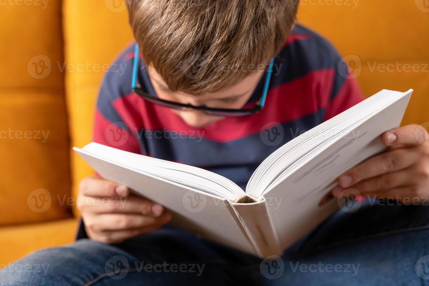 Young Schoolboy with Glasses Immersed in Book Reading on Couch photo