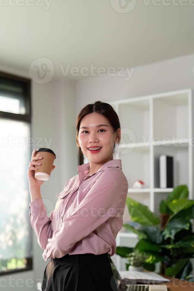 Young successful employee business woman hold takeaway craft paper cup coffee at desk at office. Achievement career concept photo