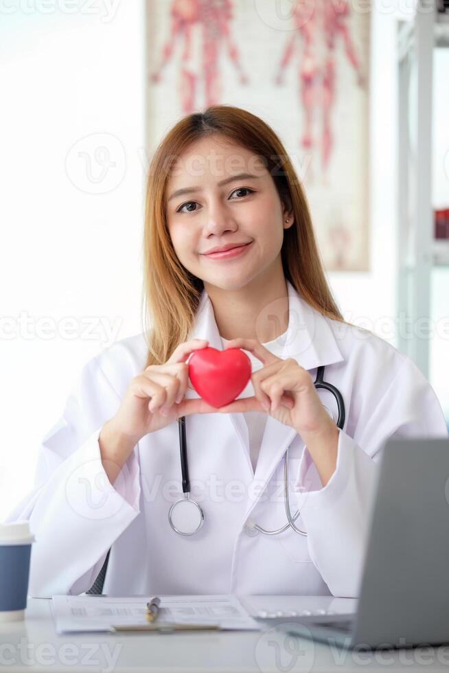 Happy young doctor woman holding red heart shape object, looking at camera with smile. Positive practitioner, cardiologist photo