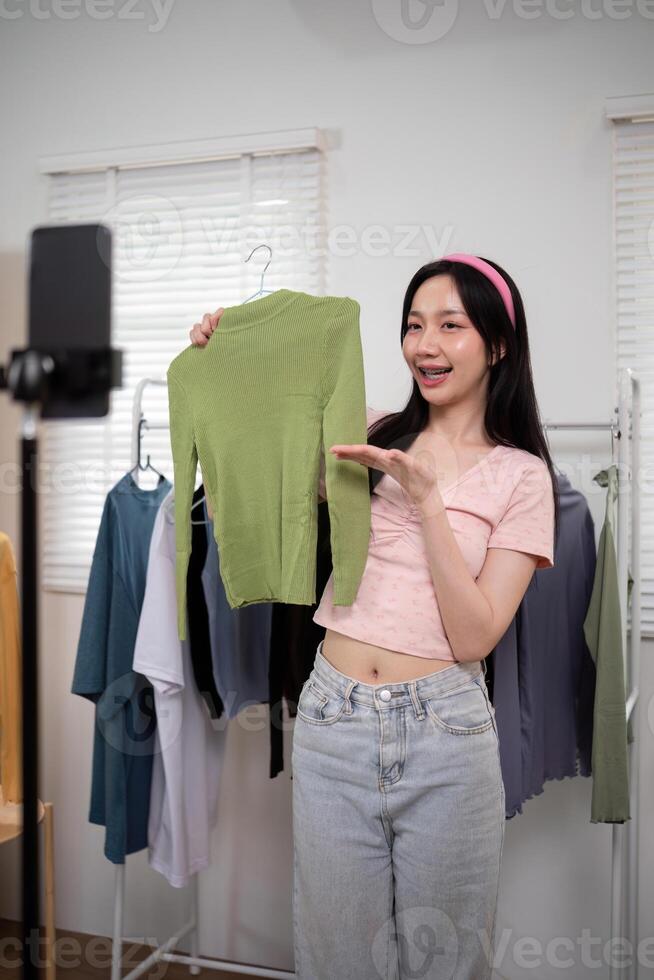 Woman asian online sell is using smartphone to broadcast live on Vlog for introduce new fashion while review shirt collection and talking with customer to selling online clothing on social media photo