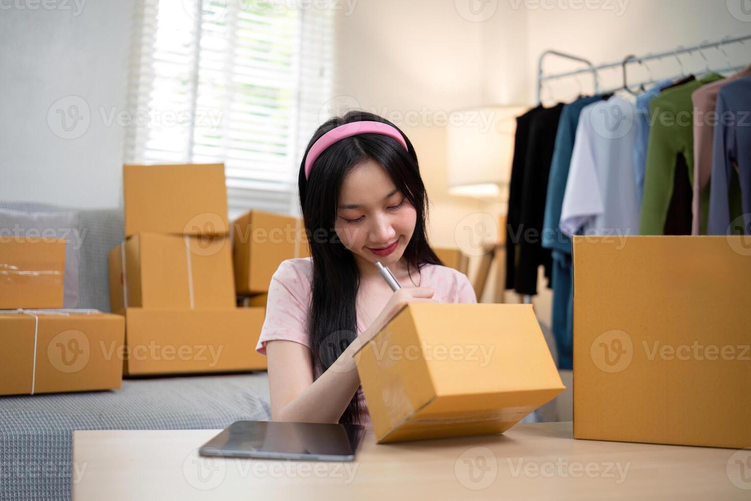 Asian woman small business entrepreneur working from home use tablet for commercial inspection. online marketing Packaging box, concept ecommerce photo