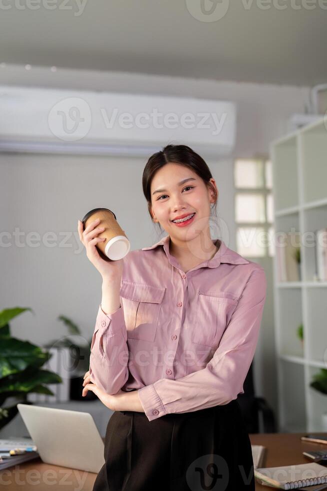 Young successful employee business woman hold takeaway craft paper cup coffee at desk at office. Achievement career concept photo