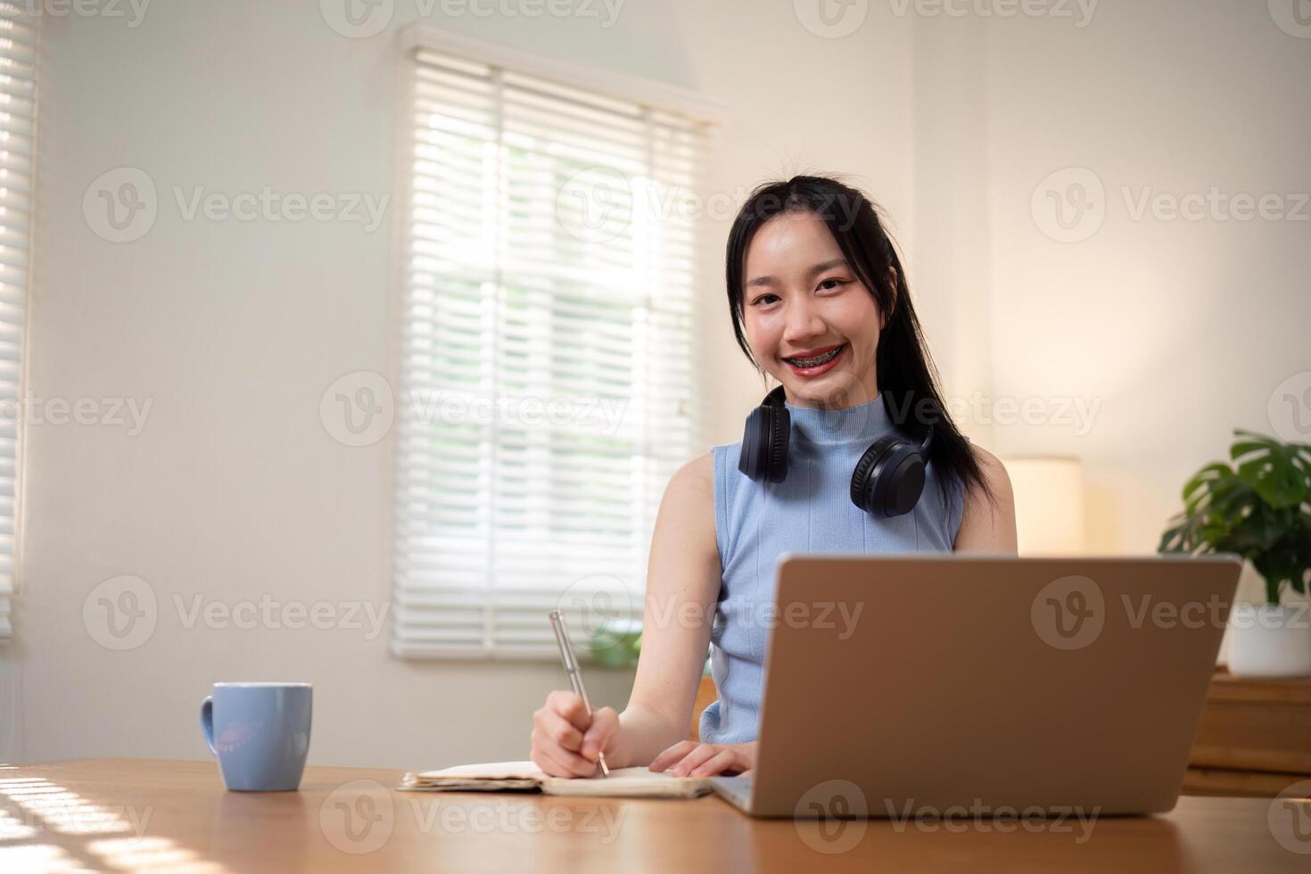 Happy young woman asian in headphones and laptop making notes, girl student talking by video conference call, online training photo