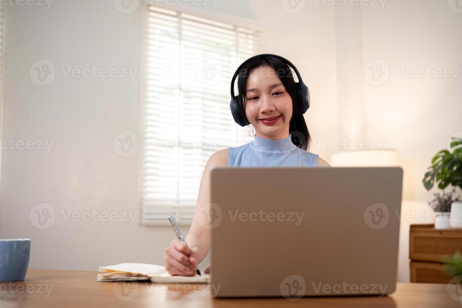 Happy young woman asian in headphones and laptop making notes, girl student talking by video conference call, online training photo