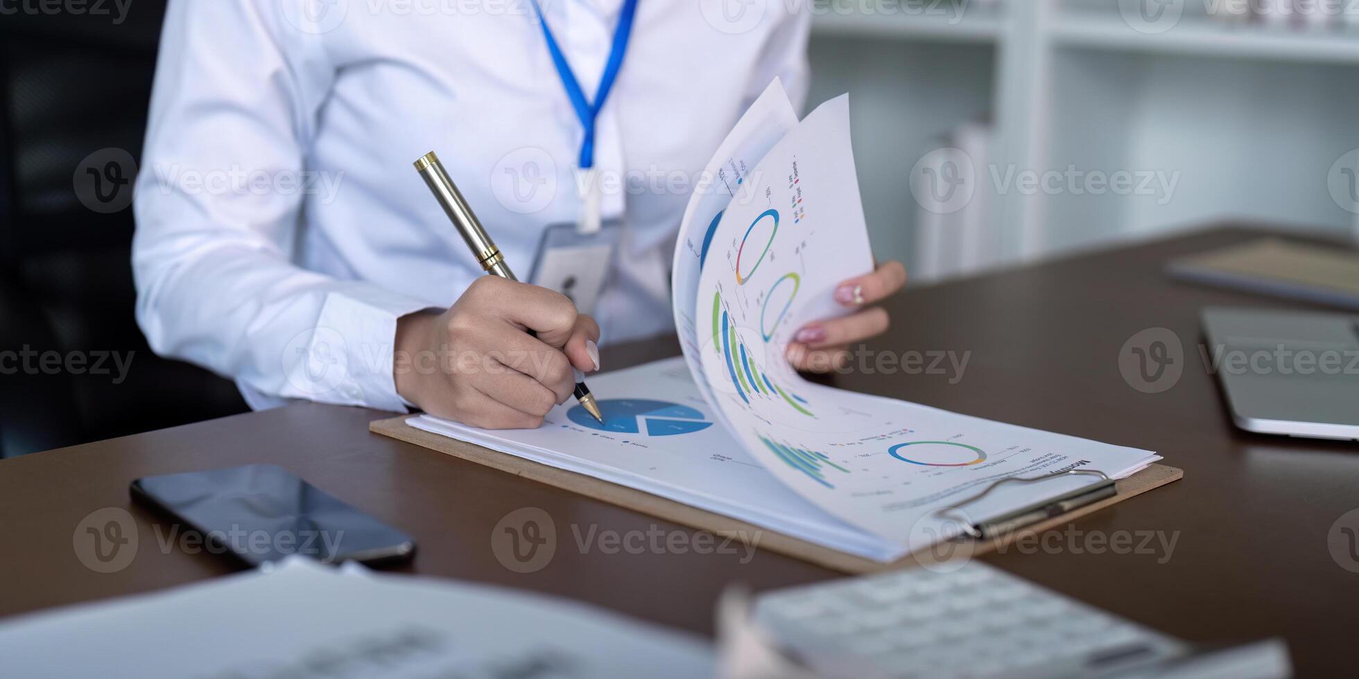Finance concept. Close up businesswoman hold a graph pen and writing report, and memo, and analyzing business documents with a laptop computer photo
