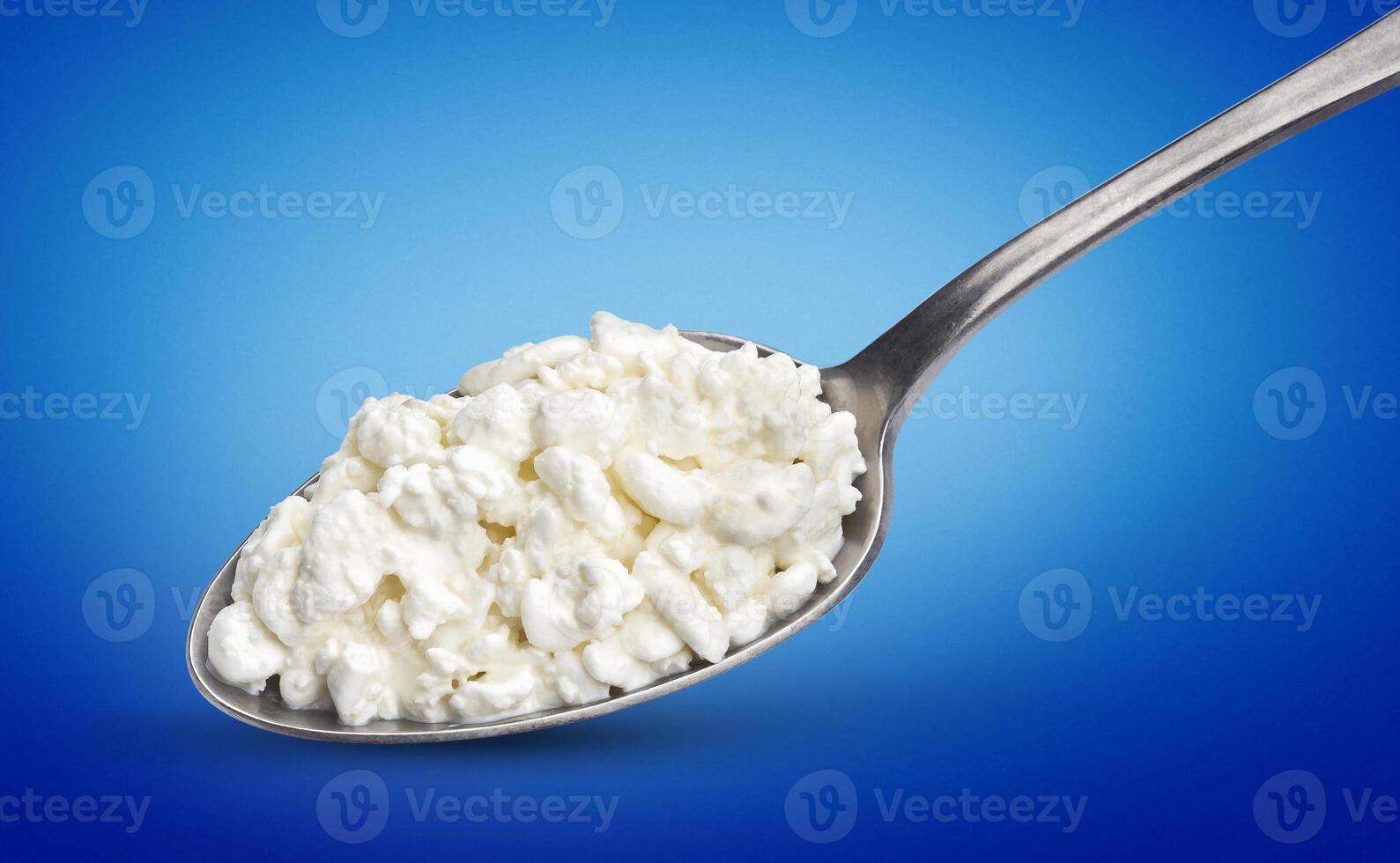 Cottage cheese in spoon isolated on blue background photo