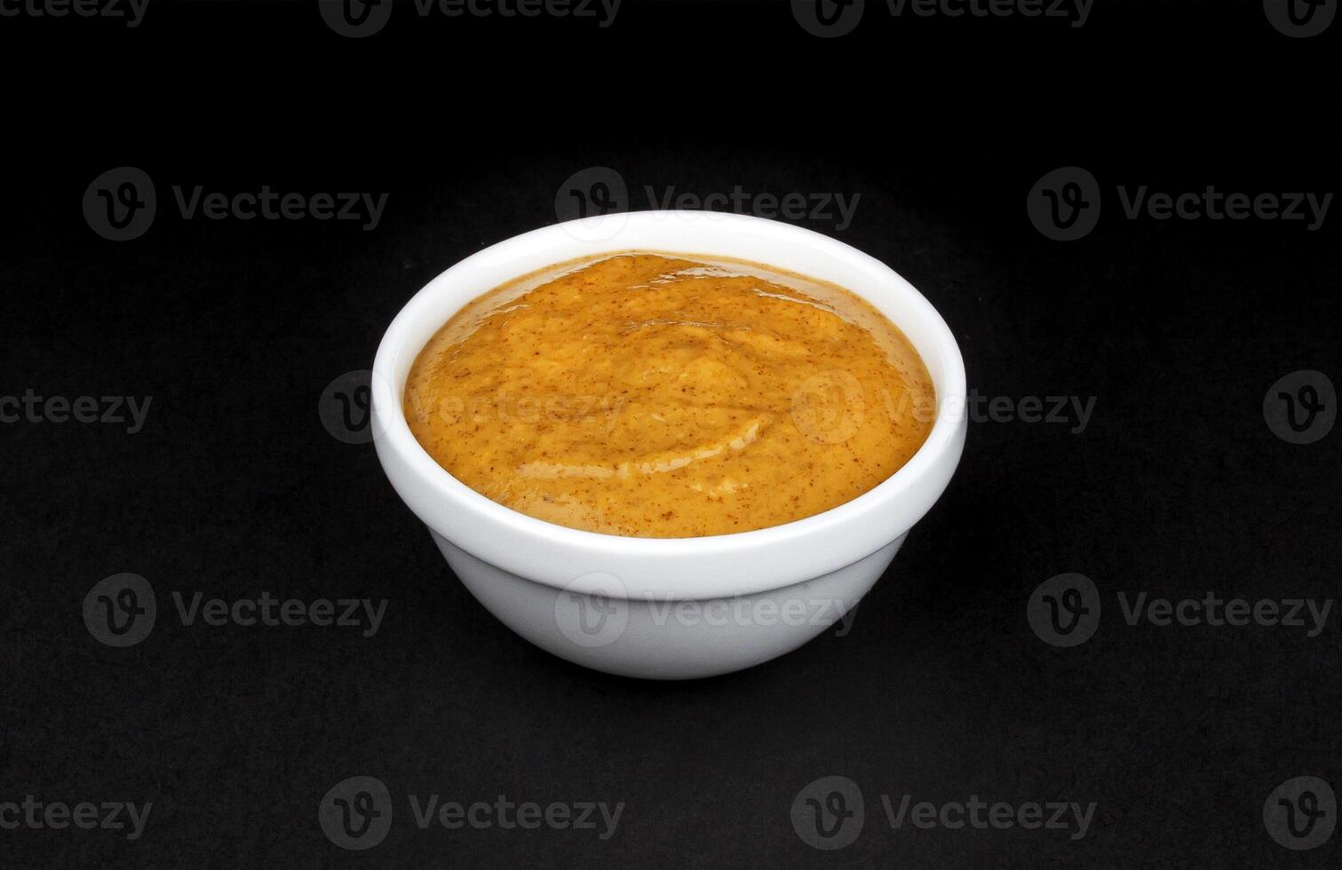 Mustard in white bowl isolated on black background photo