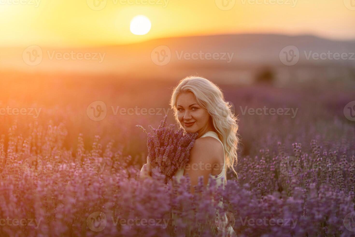 Blonde woman poses in lavender field at sunset. Happy woman in white dress holds lavender bouquet. Aromatherapy concept, lavender oil, photo session in lavender