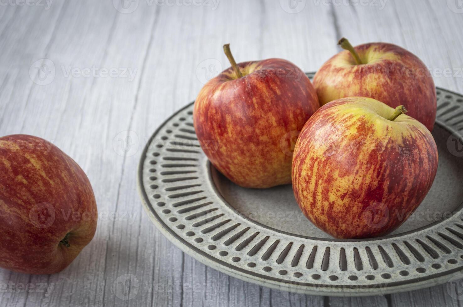 three apples are on a plate on a wooden table photo